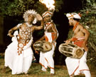 Kandyan dancer Peter Surasena adorned in full ritual costume, performing to the rhythms of the Kandyan drum, played by I.G. Sirisoma (center) and Rattota Sirisena (right), Kandy, Sri Lanka, 1987. Image © Susan A. Reed.
